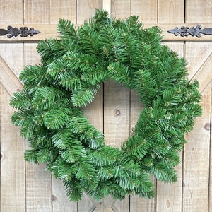 May include: A green artificial Christmas wreath made of pine branches. The wreath is hanging on a wooden door.