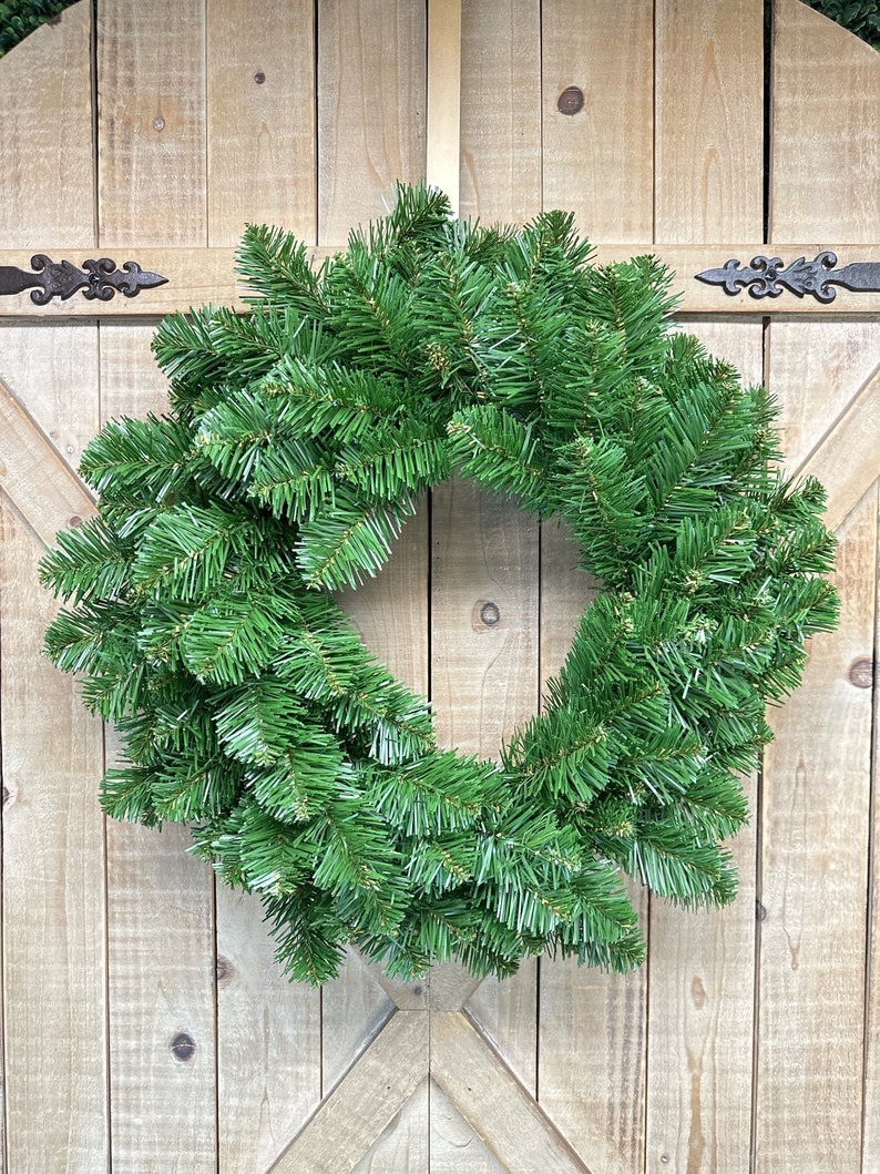May include: A green artificial Christmas wreath made of pine branches. The wreath is hanging on a wooden door.