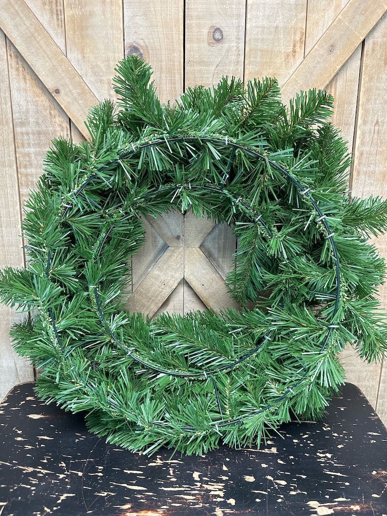 May include: A green artificial evergreen wreath with a wire frame. The wreath is on a black surface.
