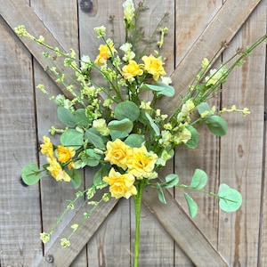 May include: A vibrant floral arrangement featuring bright yellow roses and delicate white and yellow blossoms. The bouquet includes green eucalyptus leaves and slender stems, creating a fresh, natural aesthetic. The arrangement is set against a rustic wooden backdrop.