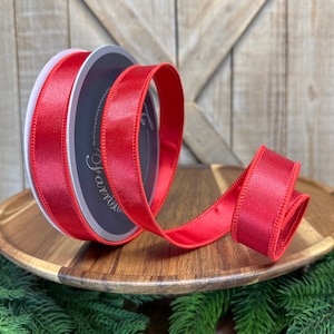 May include: A spool of red satin ribbon with a wired edge. The ribbon is wrapped around a cardboard spool with a white label that says "Satin Ribbon".