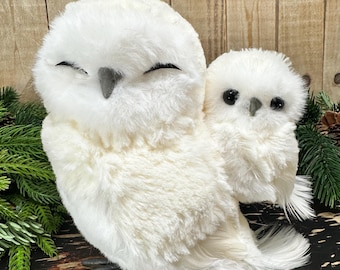 Peut inclure: Une figurine en peluche représentant deux chouettes blanches, une grande aux yeux fermés et une plus petite aux yeux sombres. Les deux oiseaux possèdent un plumage synthétique blanc et duveteux, des becs gris et des pattes grises assorties.