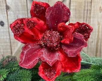 May include: A large, deep red velvet flower with glitter detailing. The flower has multiple petals and a textured centre. It is a decorative item, possibly for festive or seasonal decoration.