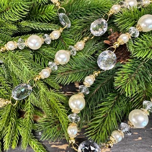 May include: A decorative garland featuring alternating white faux pearls and clear faceted crystal beads, connected by gold-toned metal links. The strand is arranged in a series of loops, showcasing the reflective surfaces of the beads.