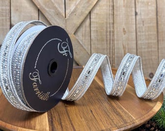 May include: A spool of silver ribbon with a metallic, textured finish and a central row of reflective, rectangular embellishments. The black spool features the white text Farrisilk and a stylized F logo, with the ribbon unspooling in a wavy pattern.