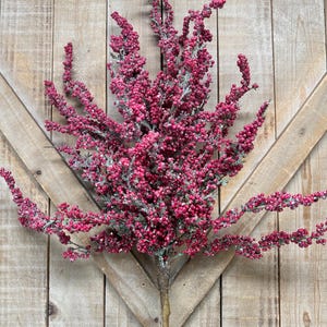 May include: A decorative floral spray featuring numerous small, vibrant magenta berries clustered on thin, branching stems. The stems and berries are lightly dusted with a white, frost-like texture, creating a winter-inspired appearance.