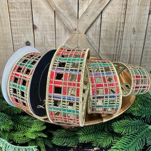 May include: A roll of decorative ribbon featuring a plaid pattern in red, green, and gold with a cut-out grid design. The ribbon has metallic gold edges and is wound around a circular spool, displaying a structured, woven texture throughout.