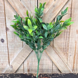 May include: A bunch of artificial green leafy stems with a wooden background.