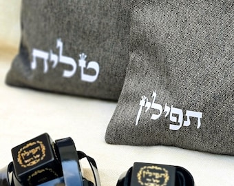 May include: Two black and gold tefillin bags with black straps, and two gray fabric bags with white Hebrew text. The text on the larger bag reads "Tefillah" and the text on the smaller bag reads "Tefillin".