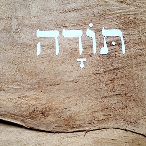 K&ouml;nnte beinhalten: Wei&szlig;e hebr&auml;ische Schrift auf einer braunen Holzoberfl&auml;che. Der Text lautet "הודיה".