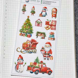 May include: A sheet of Christmas themed stickers featuring a variety of festive imagery, including a Christmas tree, Santa Claus, a snowman, a penguin, a red truck, a sleigh, and elves. The stickers are printed on white paper with a glossy finish. The text "Sweet Tea Sticker Co." is printed in the top centre of the sheet.