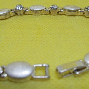 May include: A silver bracelet with oval-shaped links and clear rhinestones. The bracelet has a clasp closure.