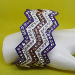 Op de afbeelding: Een set van drie armbanden in paars, wit en rood met een zigzagpatroon en strass.