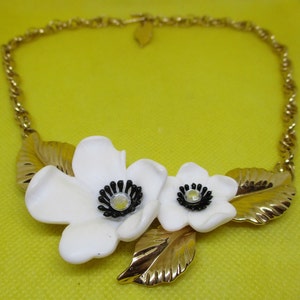 May include: A gold chain necklace with a white flower pendant. The pendant features two white flowers with black centers and gold leaves.