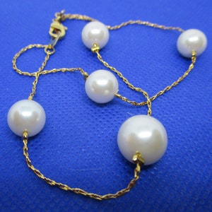 May include: A gold chain necklace with five white pearls. The chain is a delicate, twisted design.