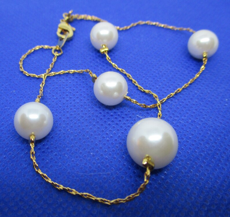 May include: A gold chain necklace with five white pearls. The chain is a delicate, twisted design.