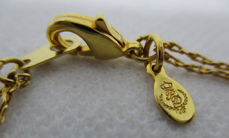 May include: Gold-tone chain necklace with a lobster clasp and a small oval tag with the inscription "R.S.D. Designs" in a cursive font.