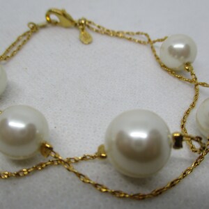 May include: A gold chain bracelet with five large white faux pearls. The bracelet has a lobster clasp closure.