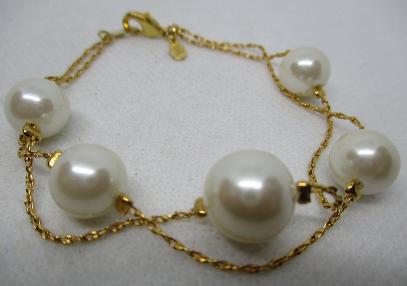 May include: A gold chain bracelet with five large white faux pearls. The bracelet has a lobster clasp closure.