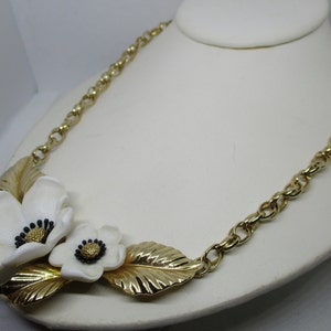 May include: A gold chain necklace with a white flower design. The flowers have black centers and are attached to gold leaves.