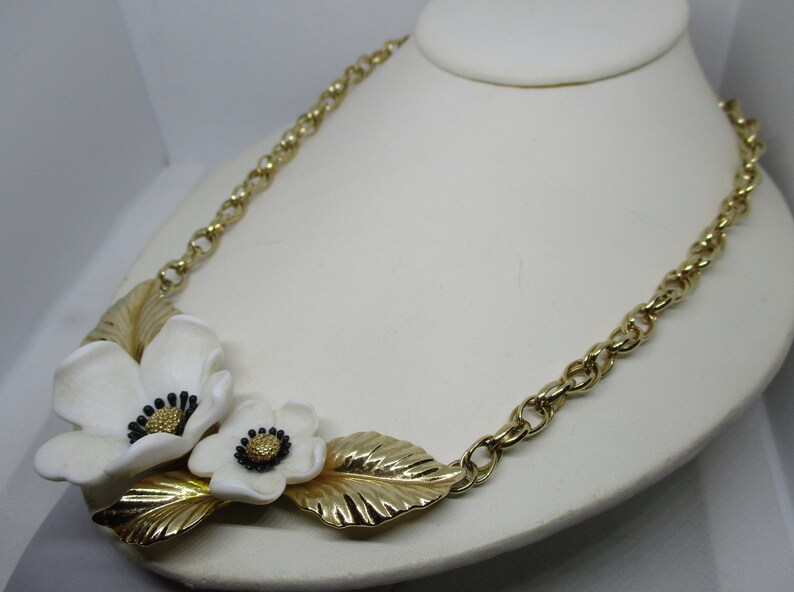 May include: A gold chain necklace with a white flower design. The flowers have black centers and are attached to gold leaves.