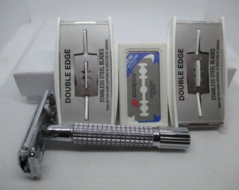 May include: A silver safety razor with a textured handle and three double-edge razor blades in individual white plastic dispensers. The dispensers have the text "Double Edge" and "Stainless Steel Blades" printed on them. One dispenser has a blue and white Dorco razor blade with the text "New Platinum SY300" printed on it.