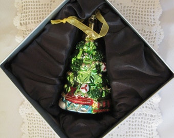 May include: A green Christmas tree ornament with red and white accents, presented in a silver box with black satin lining. The ornament has a gold ribbon for hanging. A festive holiday decoration.