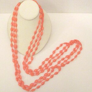 May include: A long, multi-strand necklace made of coral-coloured oval beads. The necklace is displayed on a white mannequin bust.