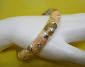 May include: A silver bangle bracelet with a multi-colored enamel design. The enamel is in shades of peach, brown, and white. The bracelet is decorated with clear rhinestones.