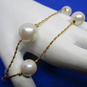 May include: A gold chain bracelet with four large white faux pearls. The chain is a delicate, twisted design.