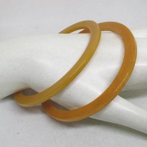 May include: Two yellow plastic bangles, one slightly larger than the other, are stacked on a white surface.
