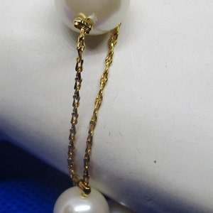May include: A gold chain bracelet with four white pearls. The bracelet is on a white surface with a blue background.
