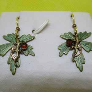 Puede incluir: Un par de pendientes de hoja verde con un pequeño lagarto y detalles de piedras preciosas rojas.