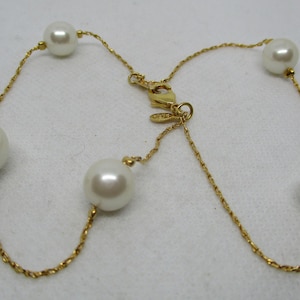 May include: A gold chain necklace with five white pearls. The chain is a twisted rope design.