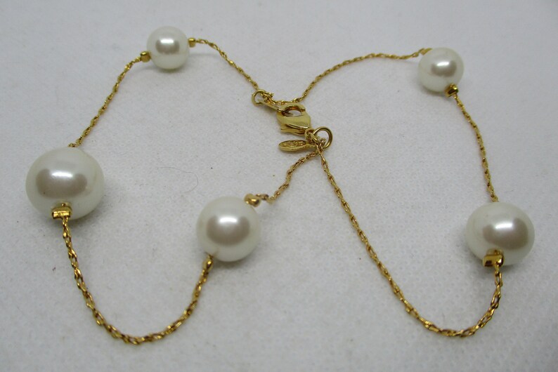 May include: A gold chain necklace with five white pearls. The chain is a twisted rope design.
