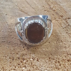 May include: A silver ring with a brown oval gemstone set in a decorative bezel. The ring has a textured band with a design on either side of the stone.