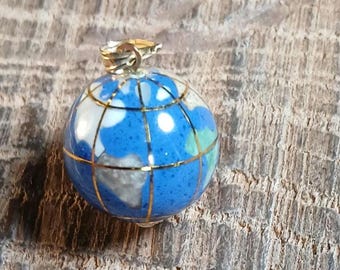May include: A spherical pendant shaped like a globe, featuring a polished blue surface inlaid with white and light green stone segments. The globe is divided by thin, gold-colored metal grid lines and includes a gold-colored metal bail at the top.