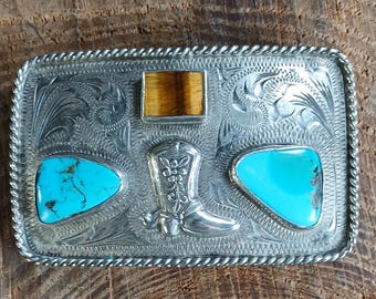 May include: Silver belt buckle with a turquoise and tiger's eye stone inlay. The buckle features a boot design and intricate floral engravings.