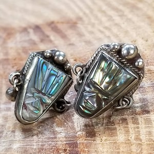 May include: A pair of silver cufflinks with abalone shell insets. The cufflinks have a geometric design and are accented with small silver beads.