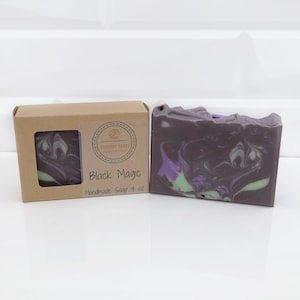May include: A bar of handmade soap with a swirling design of black, purple, and green colors. The soap is next to a small cardboard box with a window showing a matching soap sample. The box is labeled "Black Magic".
