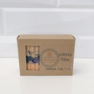 May include: A bar of handmade soap, visible through a window in a brown cardboard box. The soap has a beige base with swirls of black, green, and purple. The box is labeled "Witches Potion" and "Handmade Soap 4 oz."