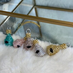 May include: Five small beaded bottle charms in different colors. The charms are light blue, pink, white, gold, and silver. Each charm has a black bead for an eye.