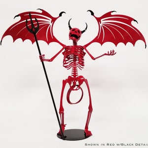 May include: Red metal skeleton sculpture of a devil with black wings and a trident. The sculpture is standing on a black base.