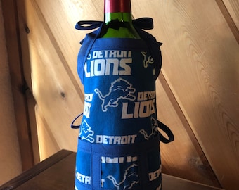 May include: A blue wine bottle holder with the Detroit Lions logo and the words "Detroit Lions" repeated throughout. The holder has a pocket on the front.