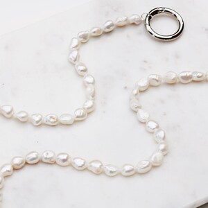 May include: A necklace made of irregular, white freshwater pearls. It has a silver-coloured clasp at one end and a gold-coloured clasp at the other. The necklace is displayed on a white marble surface.