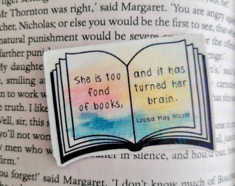 May include: A sticker in the shape of an open book with the quote "She is too fond of books, and it has turned her brain." The quote is attributed to Louisa May Alcott. The book's pages are colored in pastel hues.