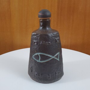 Peut inclure: Une bouteille en céramique brun foncé avec une surface texturée et un motif de poisson. La bouteille a un bouchon en liège.