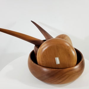 May include: A set of three wooden bowls with unique, curved handles. The bowls are nested inside each other, with the largest bowl at the bottom. The bowls are made of a light brown wood and have a smooth, polished finish.