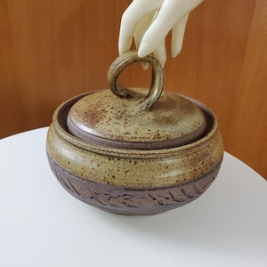 Peut inclure: Un bol de service en céramique brun et vert avec un couvercle. Le couvercle a une poignée torsadée. Le bol a un motif texturé autour du bord.
