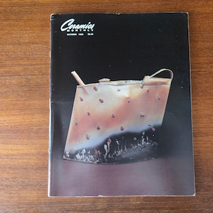 May include: The cover of "Ceramics Monthly" magazine, October 1986, features a stylized ceramic teapot. The teapot is a light brown colour with dark brown accents and a handle. The background is black and brown.